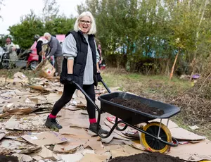 Person walking across a cardboard floor at a No Dig Meadow event with a wheelbarrow in a natural setting