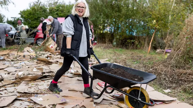 Person walking across a cardboard floor at a No Dig Meadow event with a wheelbarrow in a natural setting